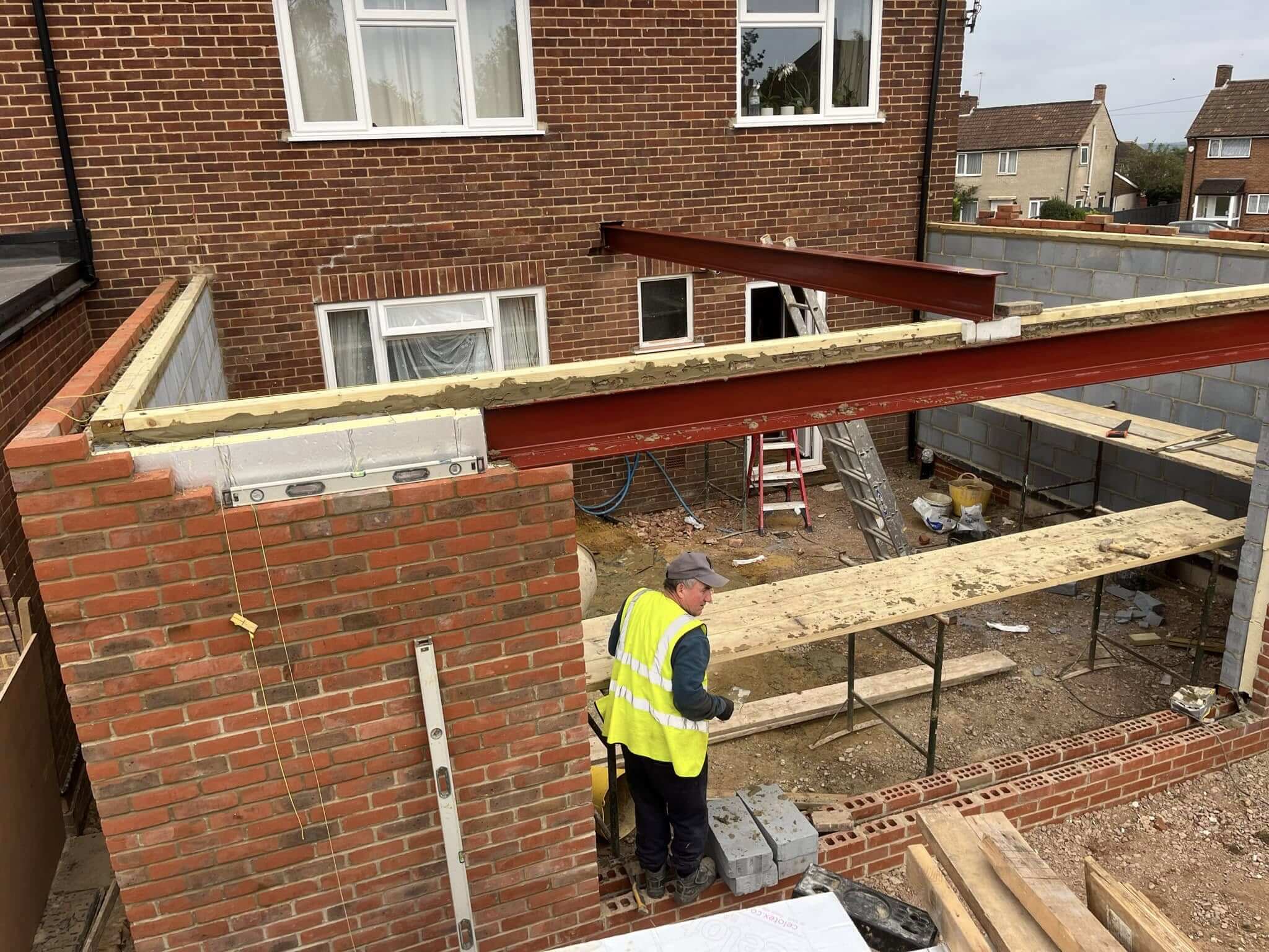 Builder in hi-vis installing a structural steel beam between two new brick walls
