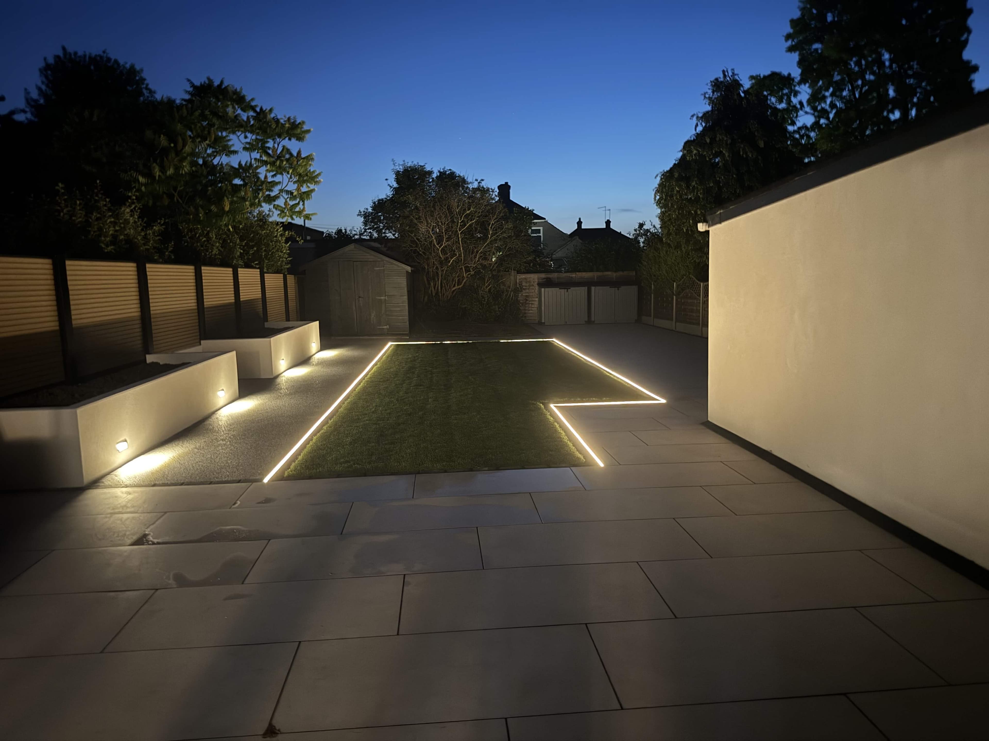 Landscaped rear garden at night with porcelain paving and recessed LED strip lighting